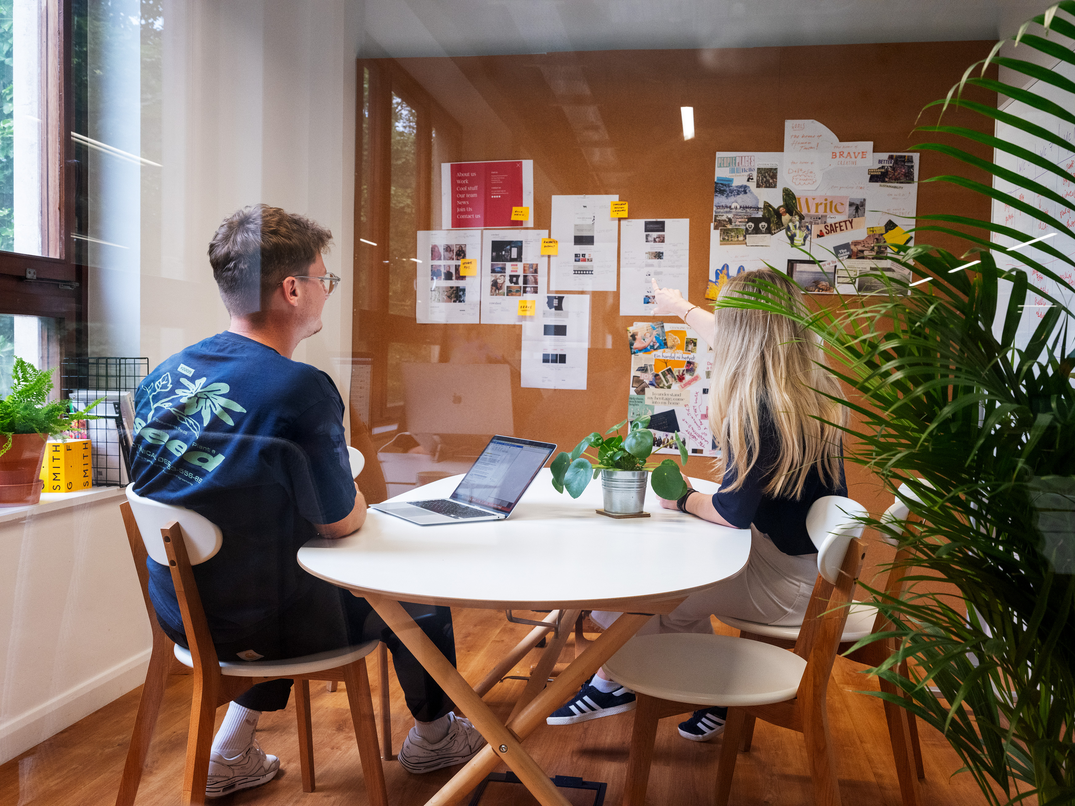 Two people sat in a modern office, pointing to some documents on a noticeboard