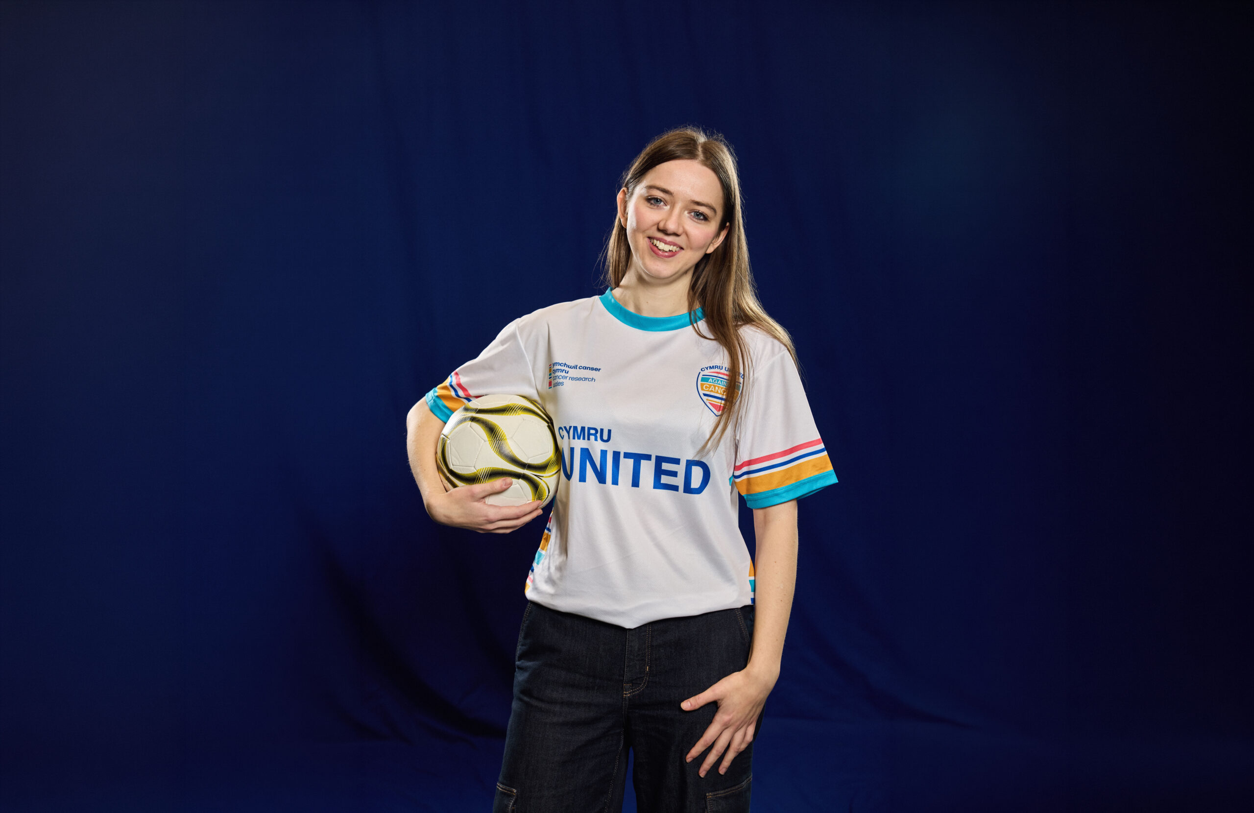 Woman holding a football, standing facing the camera, smiling.